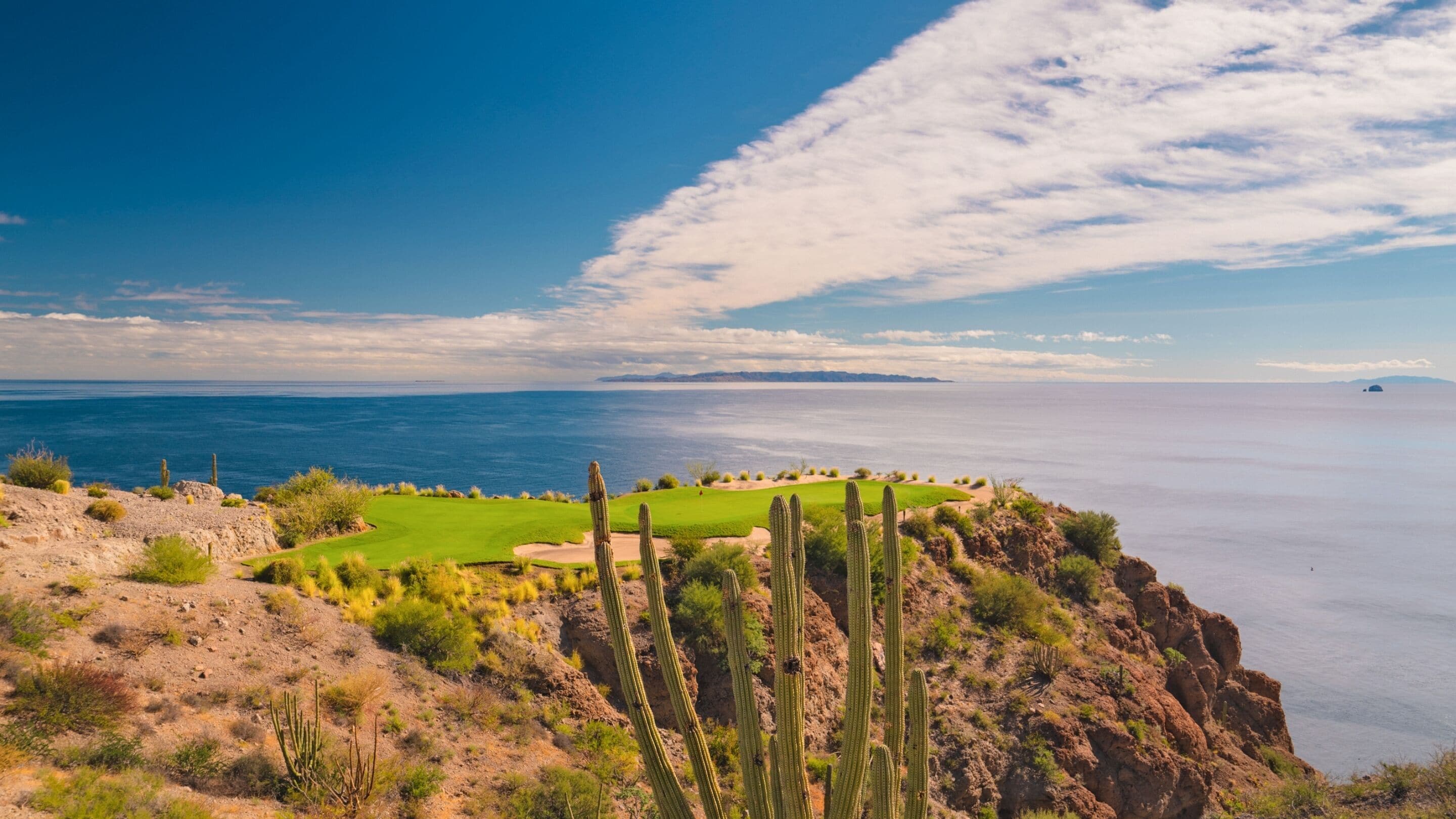 A coastal landscape with a golf course, cacti, and a view of the sea.