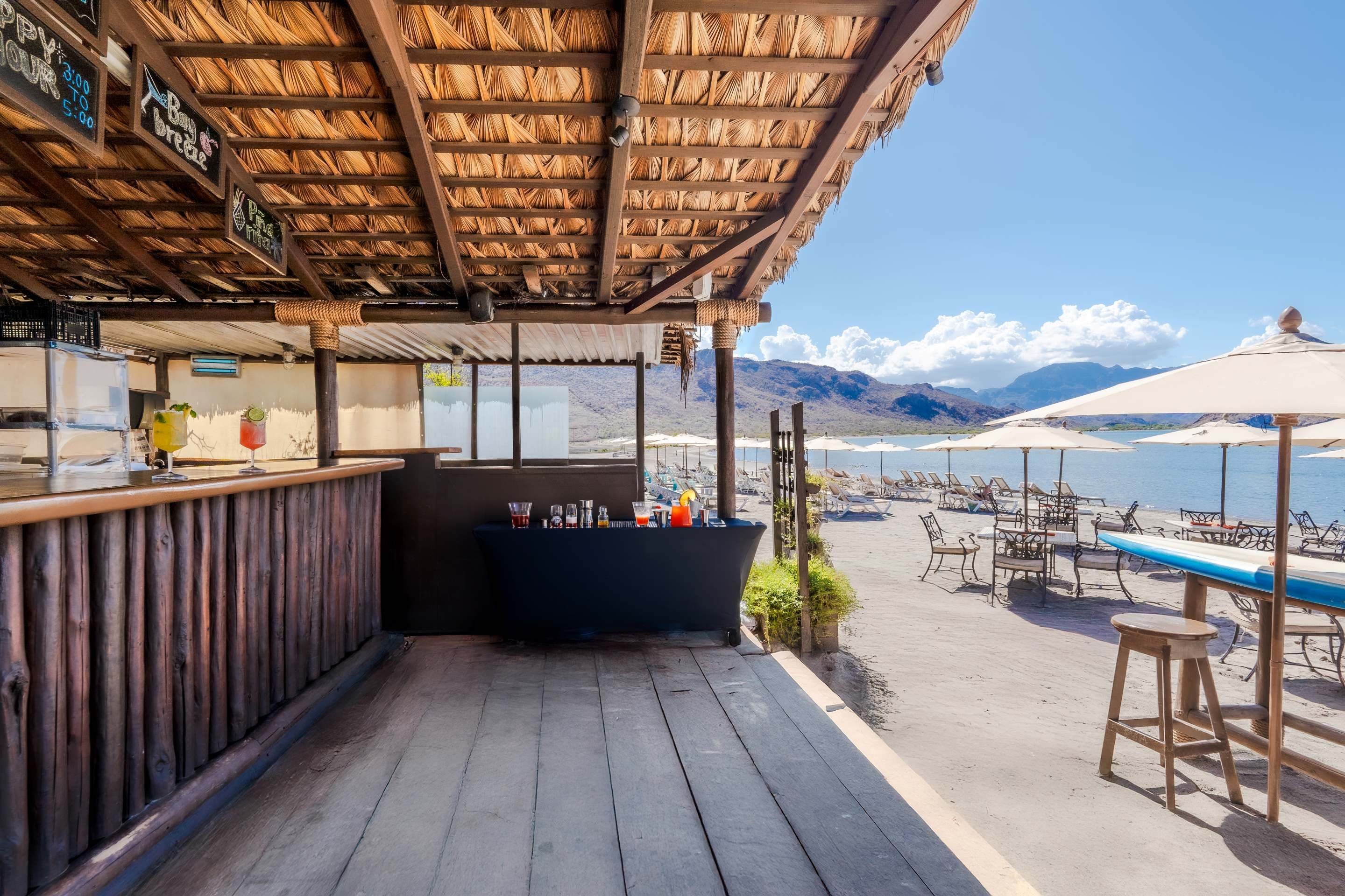 Een strandbar met rieten dak, terras en uitzicht op het strand en de bergen.