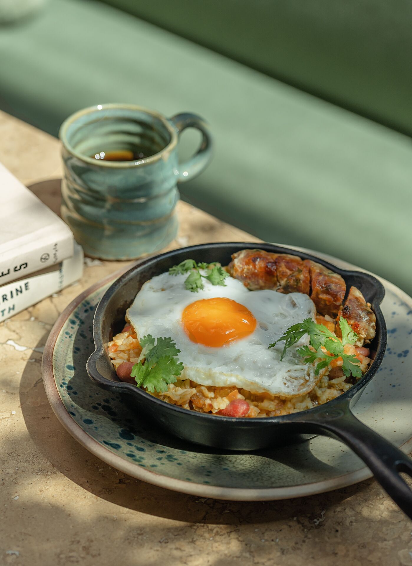 A skillet with a fried egg, rice, and vegetables on a plate, with a mug and a book in the background.