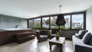 Una sala moderna con un ventanal grande, un jacuzzi integrado, dos sillones, un sofá y una mesa de centro de madera.
