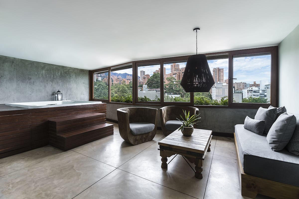 Ein modernes Wohnzimmer mit großem Fenster, einer eingebauten Whirlwanne, zwei Sesseln, einem Sofa und einem Holztisch.