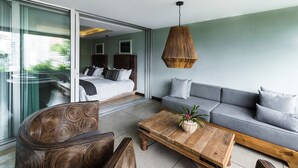 Una habitación de hotel moderna con una cama grande, un sofá gris, una mesa de centro de madera y una lámpara colgante de mimbre.