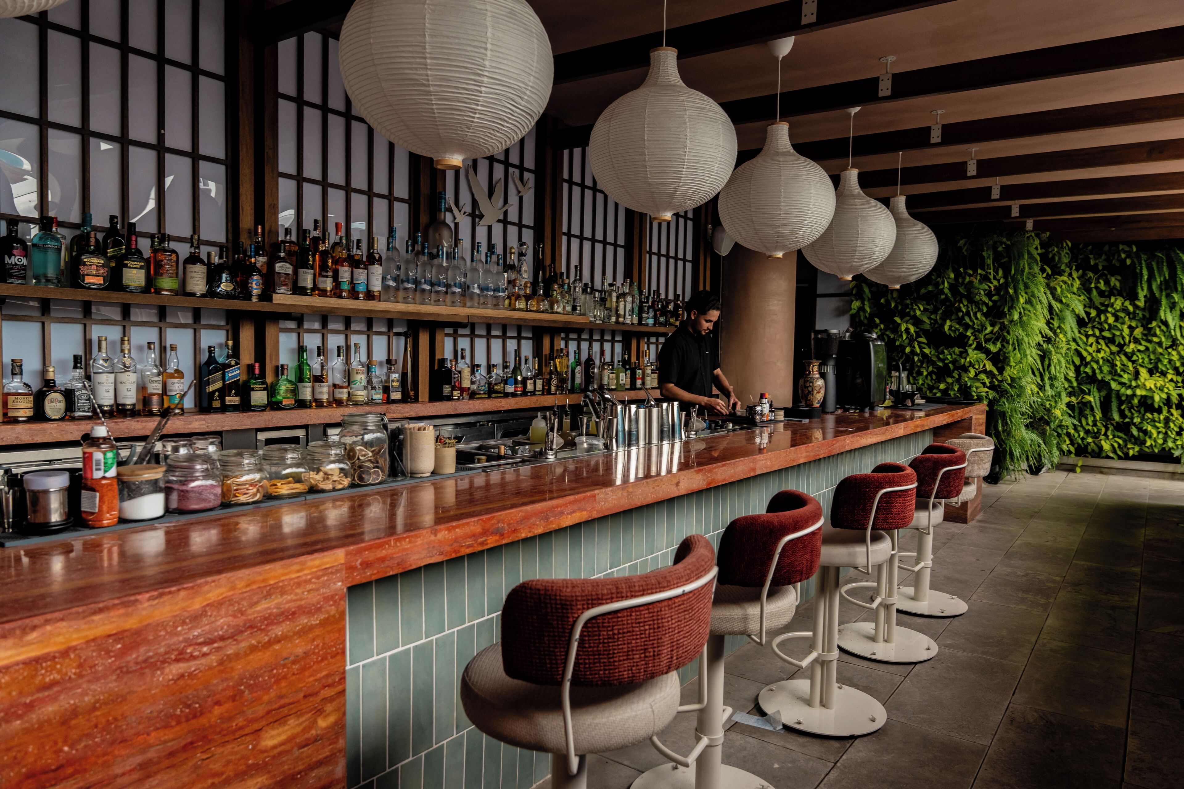 A bar area with a wooden counter, multiple liquor bottles, and hanging paper lanterns.