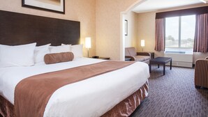 A hotel room with a large bed, a desk, a chair, and a view of the outside through a window. - Ramada by Wyndham Estevan (Estevan)