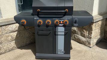 A black outdoor grill with four burners, a side shelf, and a water tank.