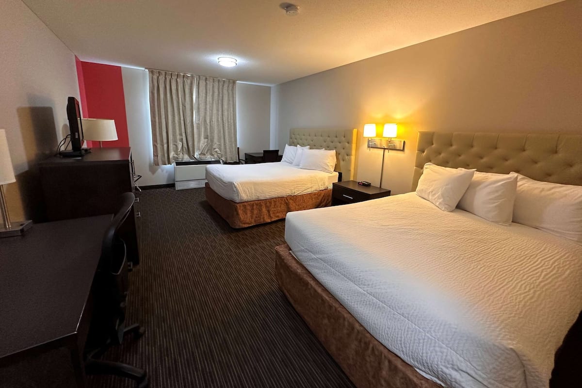 A hotel room with two beds, a desk, a chair, a lamp, and a window with curtains.
