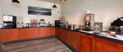 Una cucina moderna con mobili in legno, una macchina per il caffè, una piastra per waffle e un distributore automatico di caffè.