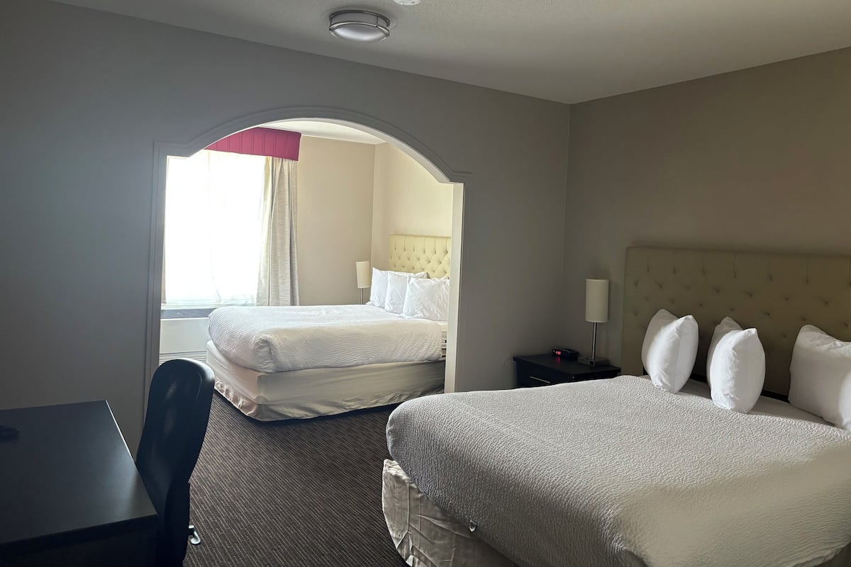 A hotel room with two beds, a desk, and a window with curtains.