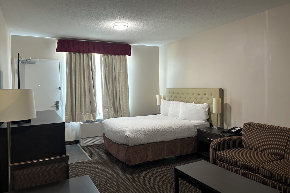 A hotel room with a bed, a desk, a chair, a lamp, and a window with curtains.