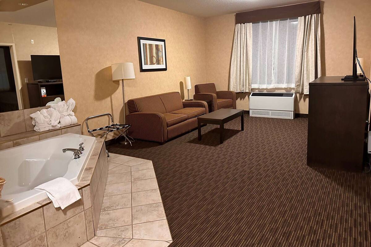 A hotel room with a large bathtub, a sofa, a coffee table, and a television.