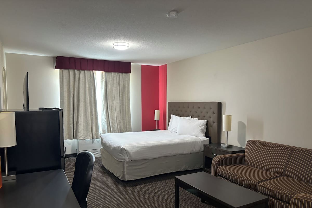 A hotel room with a bed, a desk, a chair, a sofa, and a TV.