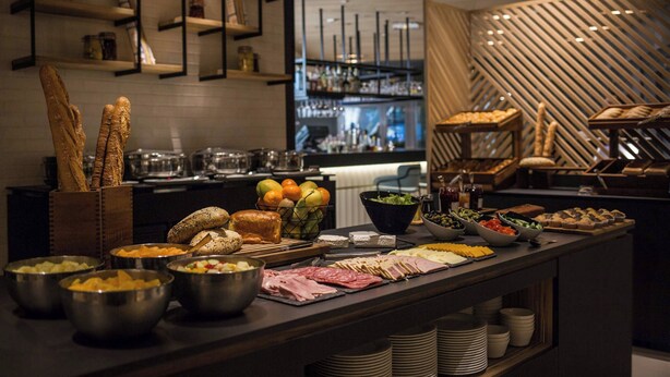 A buffet with various food items and a bar area in the background. - Courtyard by Marriott Paris Arcueil (Arcueil)