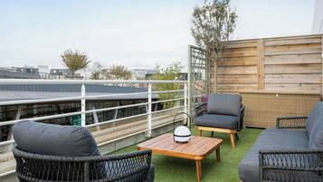 En tagterrasse med fletmøbler, et lille bord og udsigt til bygninger i baggrunden.
