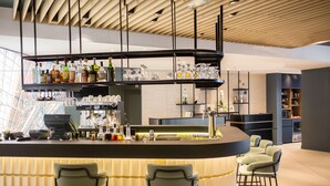 A modern bar area with a curved counter, multiple shelves of bottles, and bar stools. - Courtyard by Marriott Paris Arcueil (Arcueil)