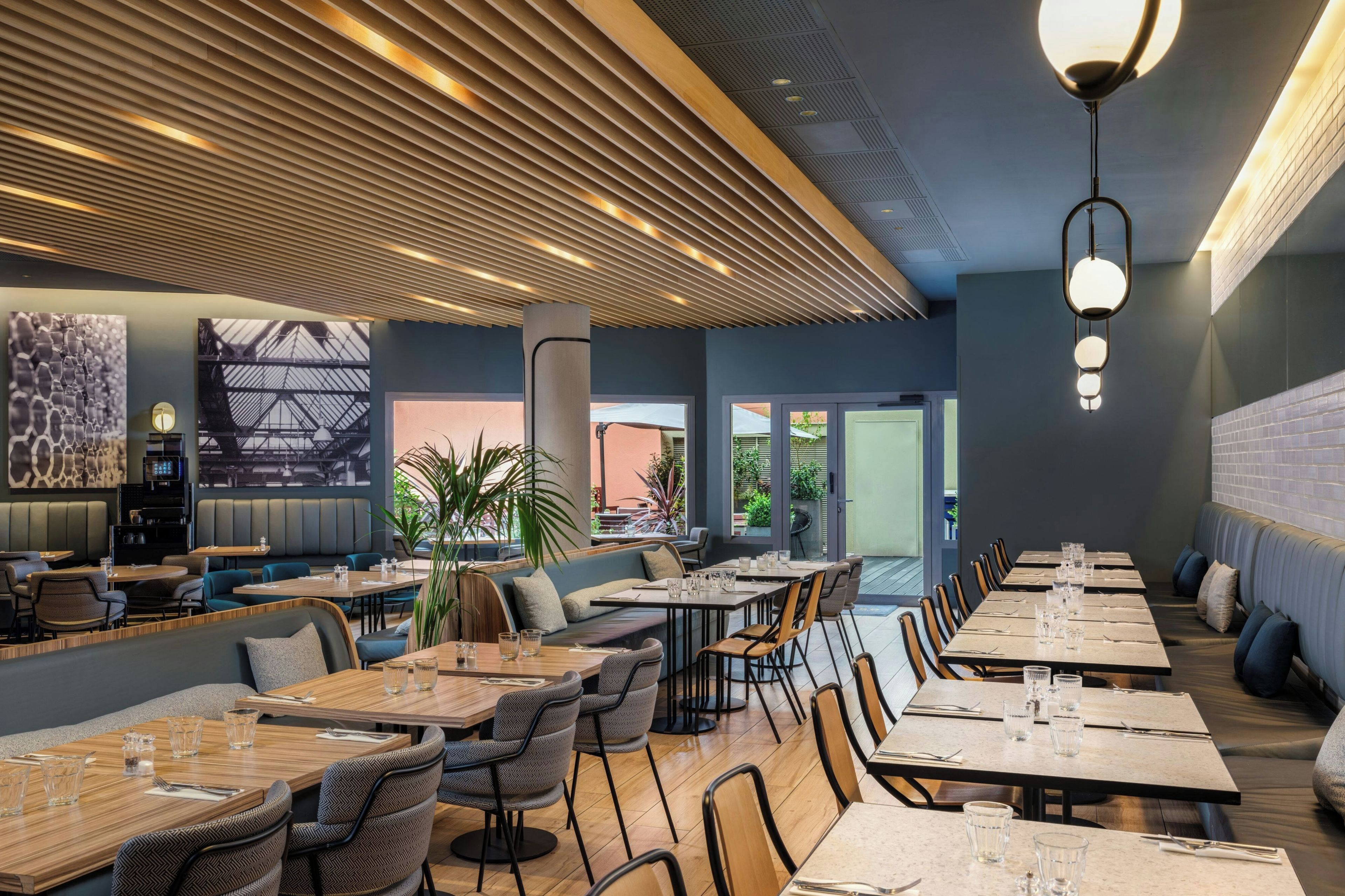 A modern restaurant interior with high ceilings, wooden slats, and a mix of seating arrangements including tables and booths.