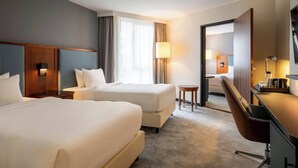 A hotel room with two beds, a desk, a chair, a lamp, and a view of the hallway. - Courtyard by Marriott Paris Arcueil (Arcueil)