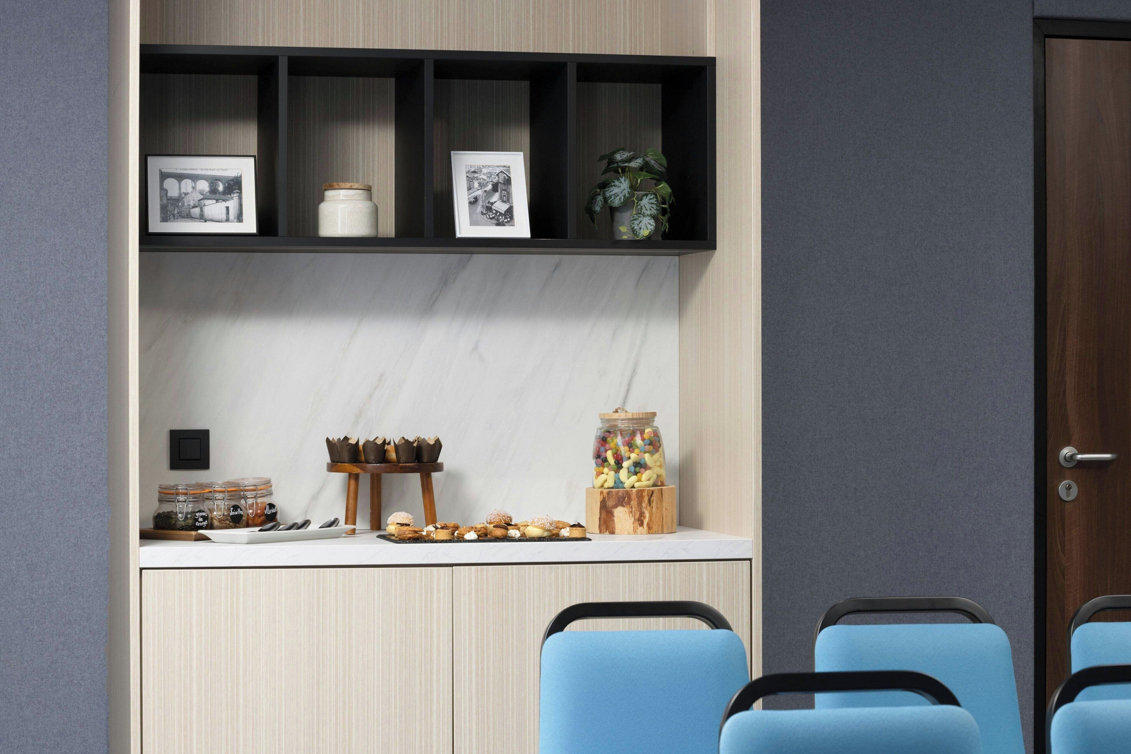 A modern room with a kitchen area, a seating area with blue chairs, and a door.