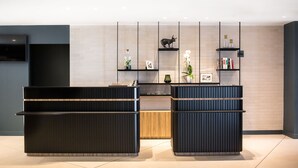 A modern reception area with a black reception desk, a flat-screen TV mounted on the wall, and a decorative shelf with various items. - Courtyard by Marriott Paris Arcueil (Arcueil)