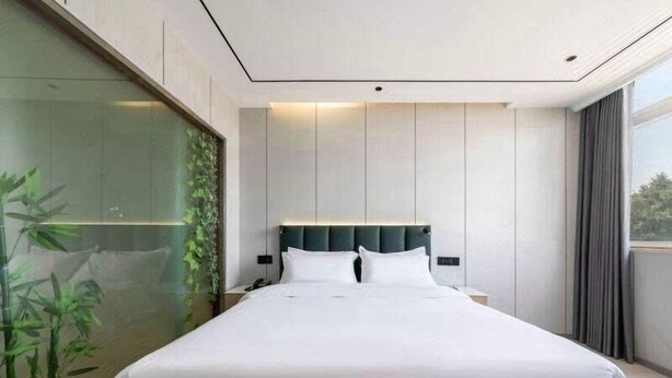 A modern hotel room with a large bed, a nightstand, and a glass wall with greenery. - GreenTree Inn Huaian Chuzhou Dadao Hotel (Huai'an)