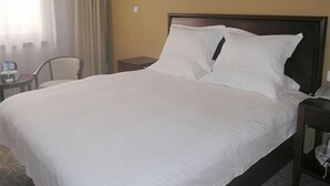 A hotel room with a large bed, a bedside table, a chair, and a window with curtains.
