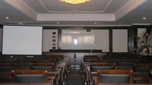 A theater with rows of wooden seats, a large screen, and a chandelier.