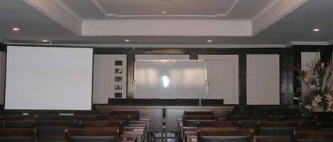 A theater with rows of wooden seats, a large screen, and a chandelier.