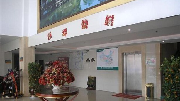 A lobby with a round table, potted plants, and a large screen displaying a scenic image.