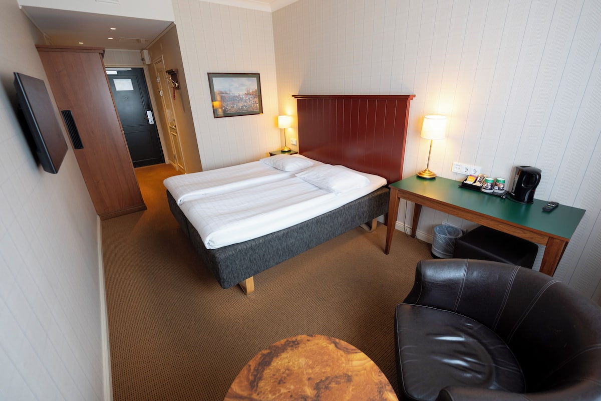 Une chambre d’hôtel avec un lit, un bureau, une chaise, une télévision et une lampe.