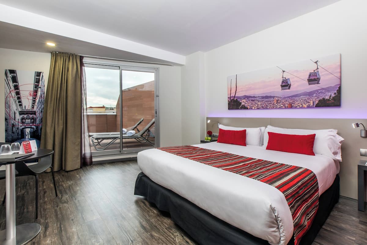 Ein Hotelzimmer mit einem großen Bett, einem Schreibtisch mit Stuhl, einem Balkon mit Blick auf die Stadt und einem Gemälde der Stadtlandschaft mit Straßenbahnen.