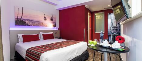 A hotel room with a bed, a TV mounted on the wall, a table with breakfast items, and a painting of a cable car on the wall.