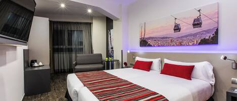 Habitación de hotel moderna con una cama grande, zona de estar y un cuadro de un paisaje urbano en la pared.