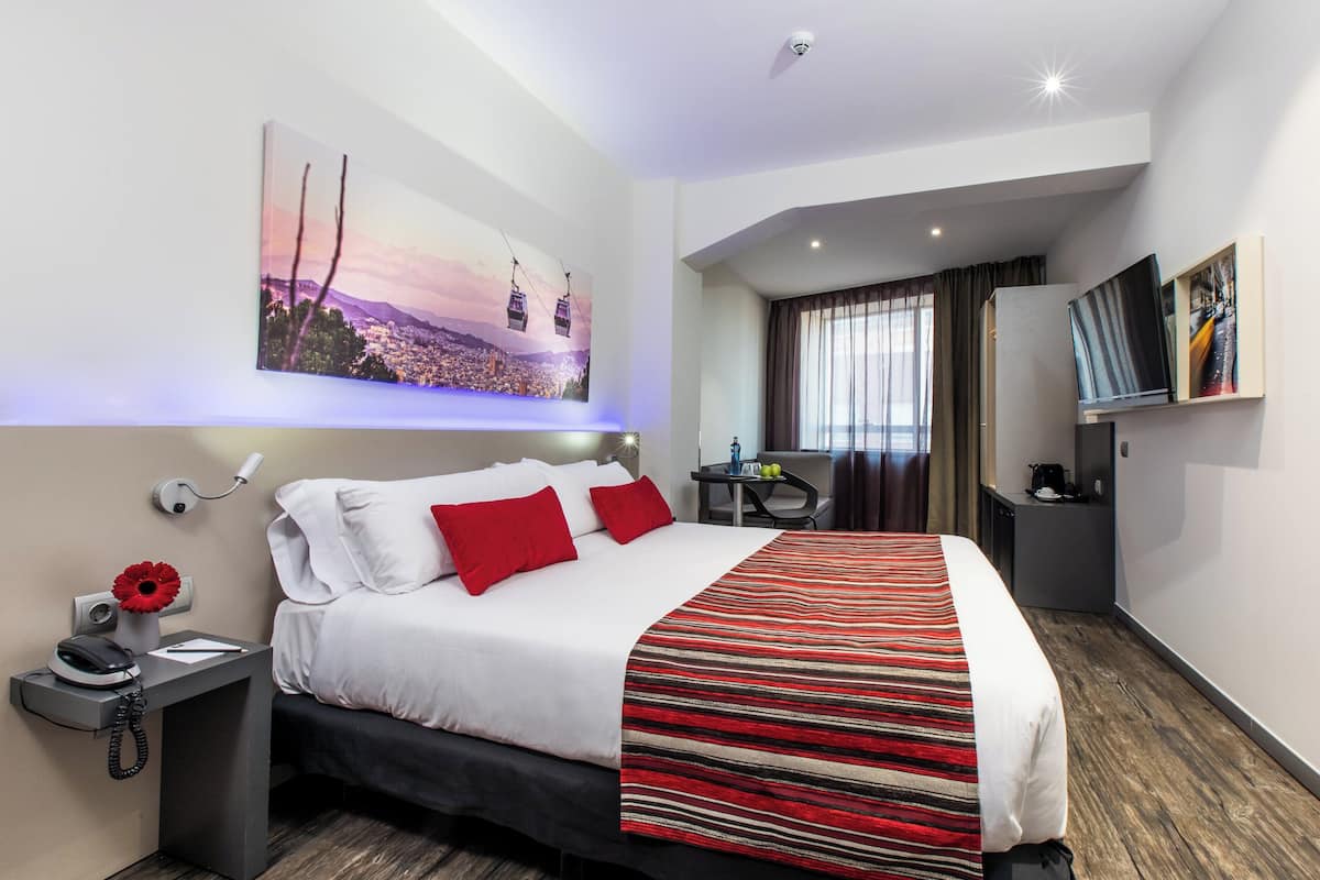 Ein Hotelzimmer mit einem großen Bett, einem Schreibtisch, einem Sessel, einem Fernseher und einem Bild an der Wand.