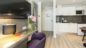 A modern kitchen with white cabinets, a microwave, and a coffee maker. There is a dining area with a purple chair and a table.
