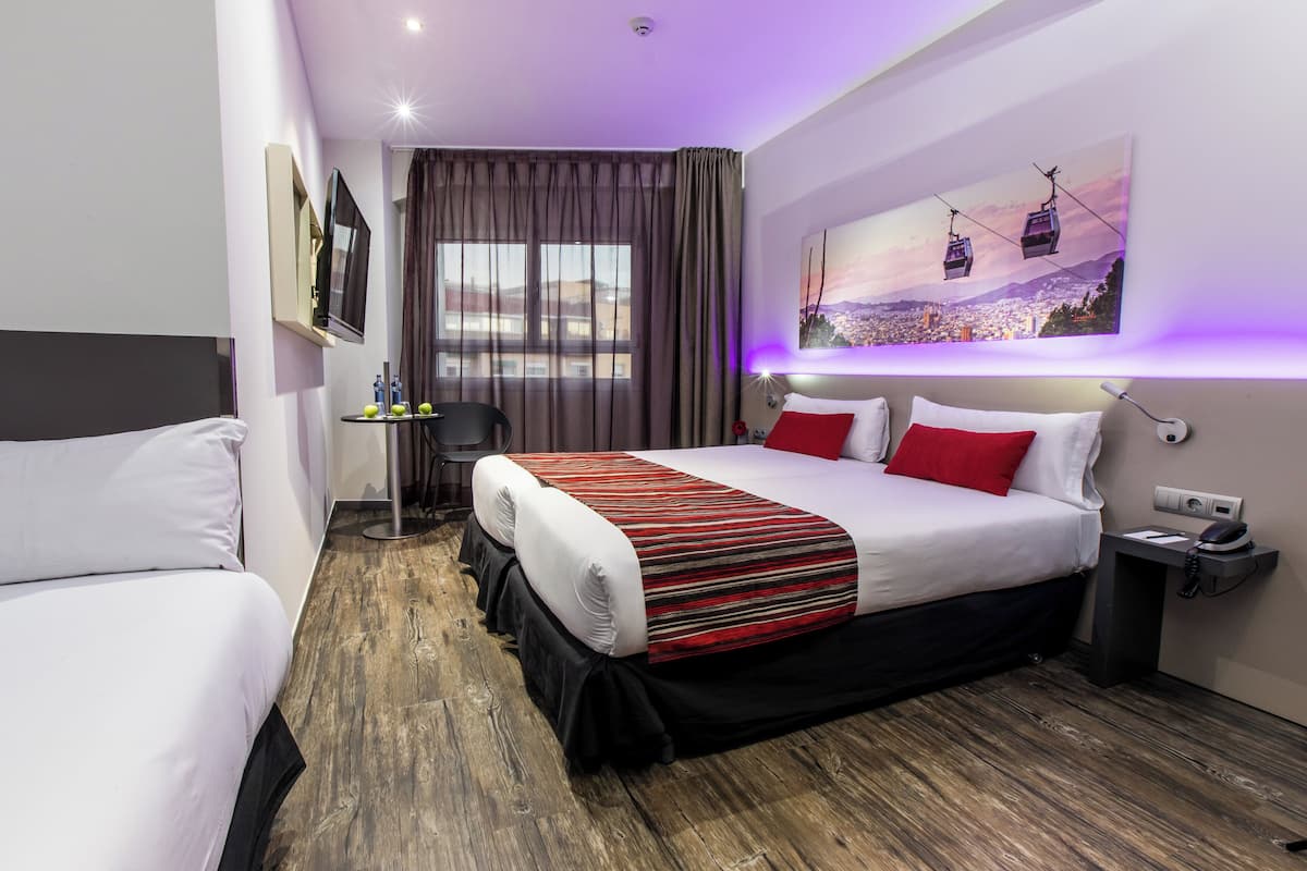 Ein Hotelzimmer mit einem großen Bett, einem Einzelbett, einem Schreibtisch mit Stuhl, einem Fenster mit Vorhängen und einem Stadtbild an der Wand.