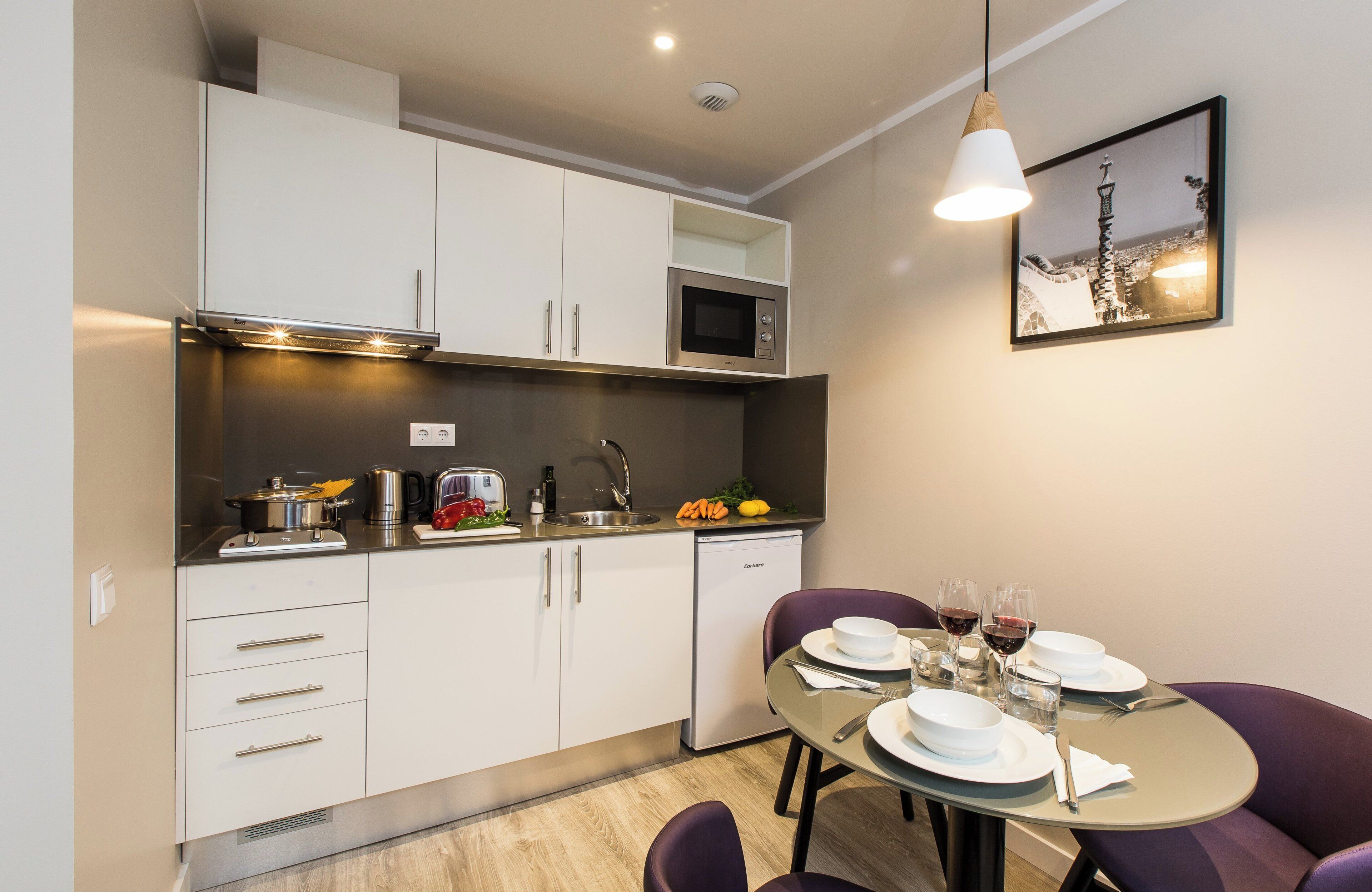 Una cocina moderna con armarios blancos, microondas integrado y una zona de comedor con una mesa dispuesta para dos personas.