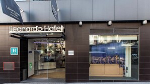 The exterior of the Leonardo Hotel with a modern facade, a glass entrance, and a visible seating area inside.