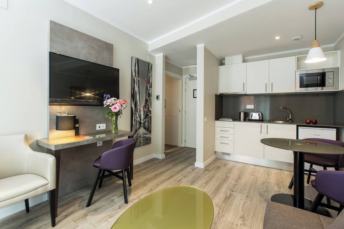 A modern kitchen with white cabinets, a microwave, and a dining area with a green table and purple chairs.