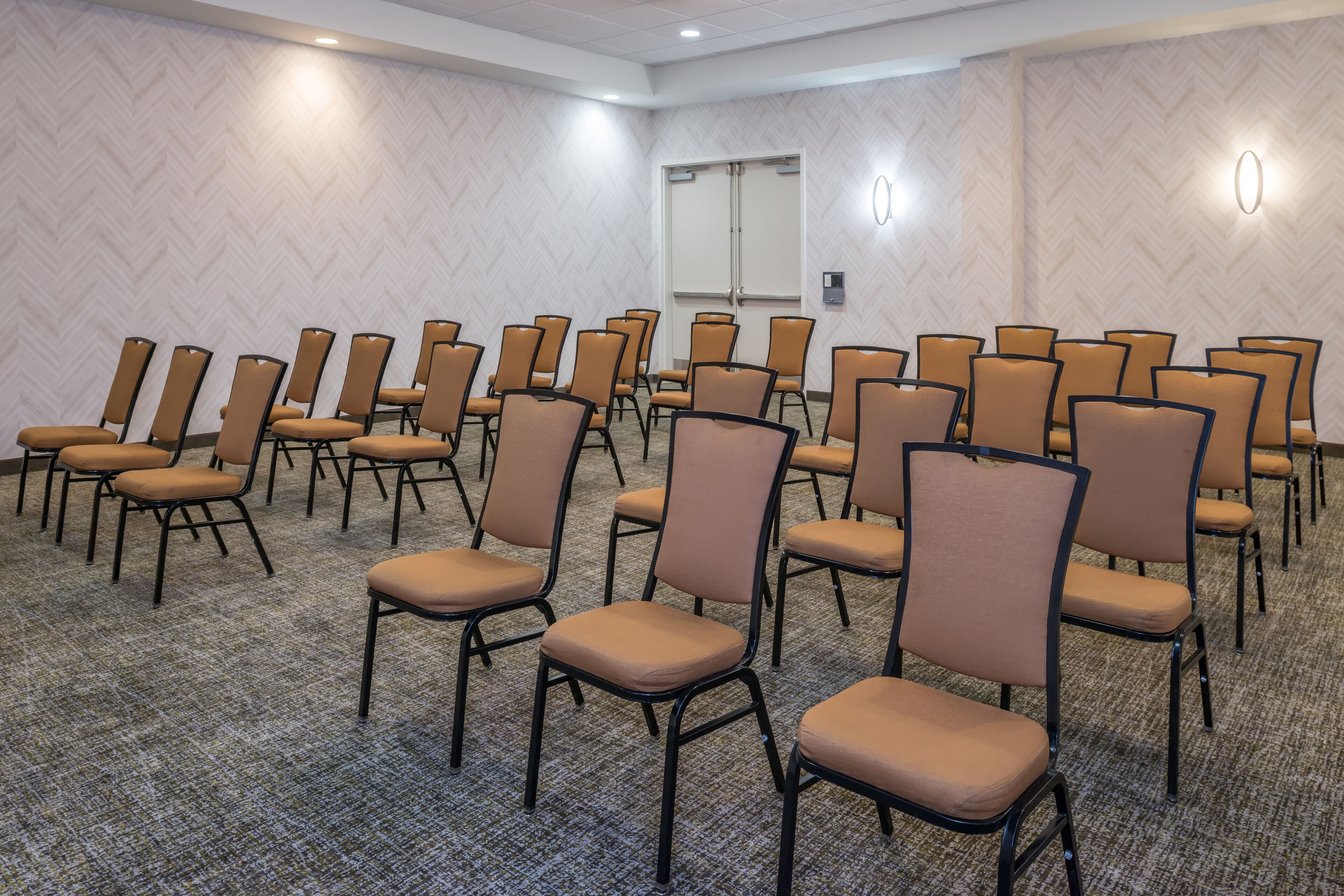 A conference room with rows of chairs, carpeted floor, and a door in the background.