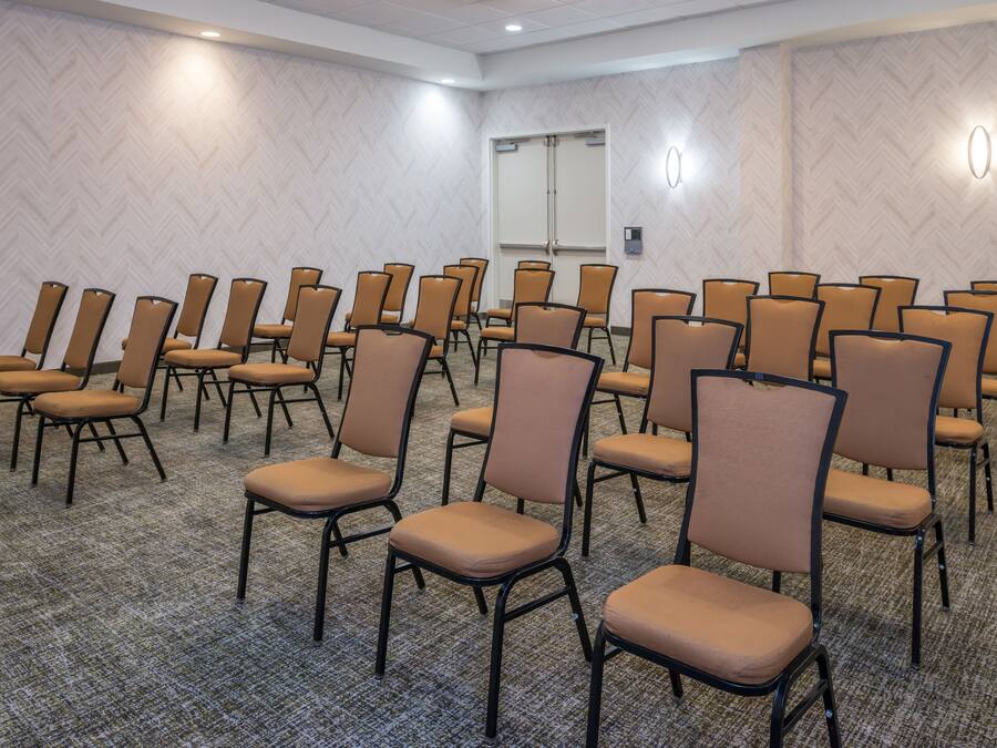 A conference room with rows of chairs, carpeted floor, and a door in the background.