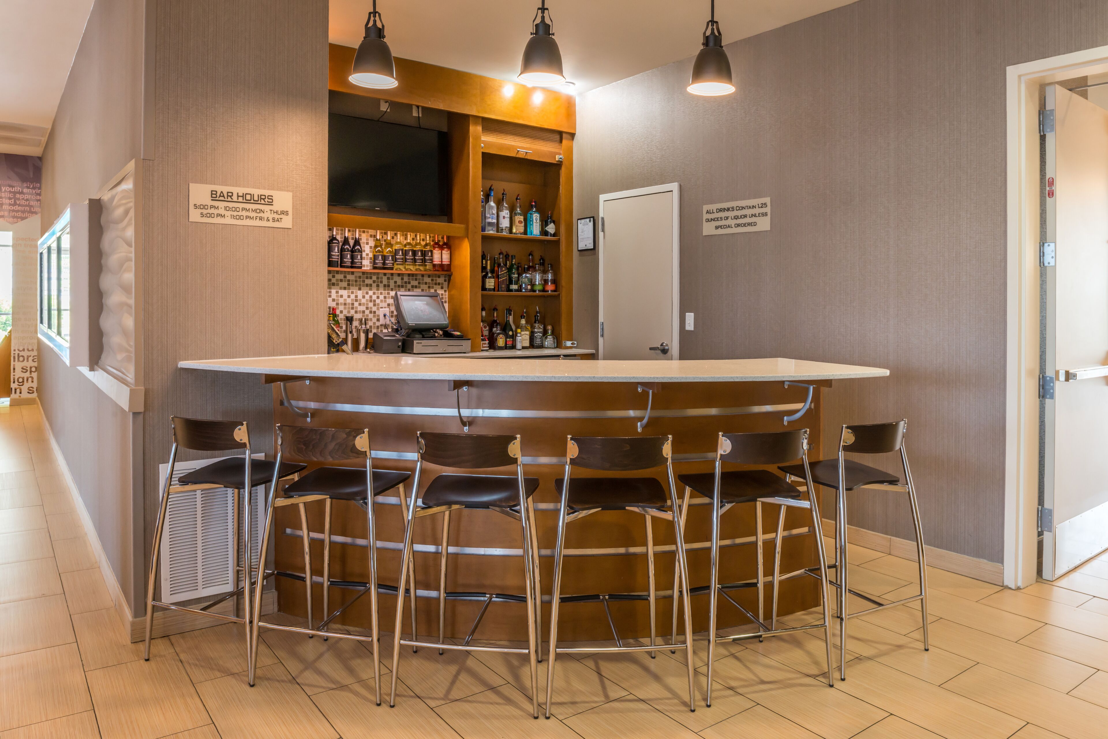 Un espace bar avec des tabourets, un comptoir et un panneau indiquant les heures d’ouverture du bar.