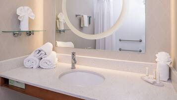 A hotel bathroom with a round mirror, a sink, and neatly folded towels on the counter.