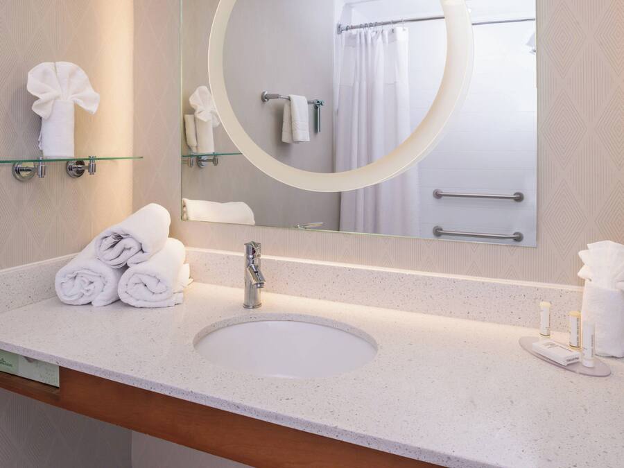 A hotel bathroom with a round mirror, a sink, and neatly folded towels on the counter.