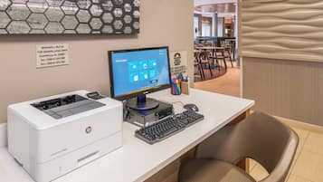 A hotel reception desk with an HP printer, a computer monitor, and a keyboard. There is a sign with the hotel's address and contact information.
