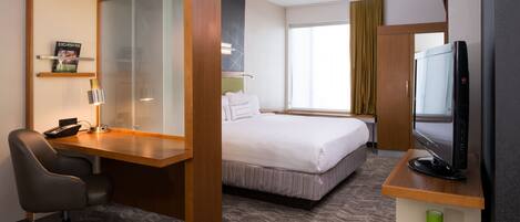 Una habitación de hotel con una cama, un escritorio con computadora, una silla, televisor y una ventana con cortinas.