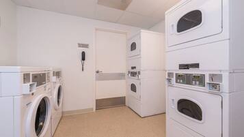 A laundry room with multiple washing machines and dryers, a door with a phone, and a sign for assistance.