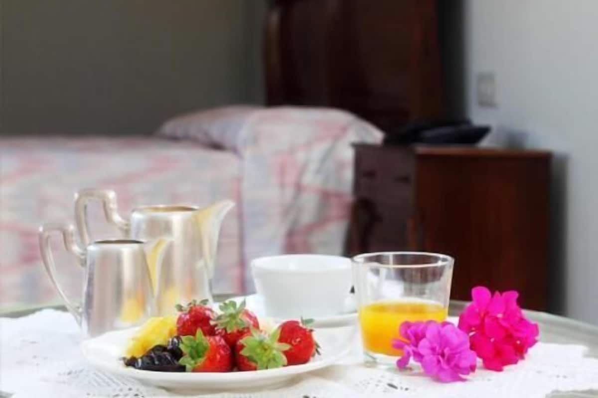 Une table de petit-déjeuner bien dressée, avec une carafe, une assiette de fruits, un verre de jus et une tasse.
