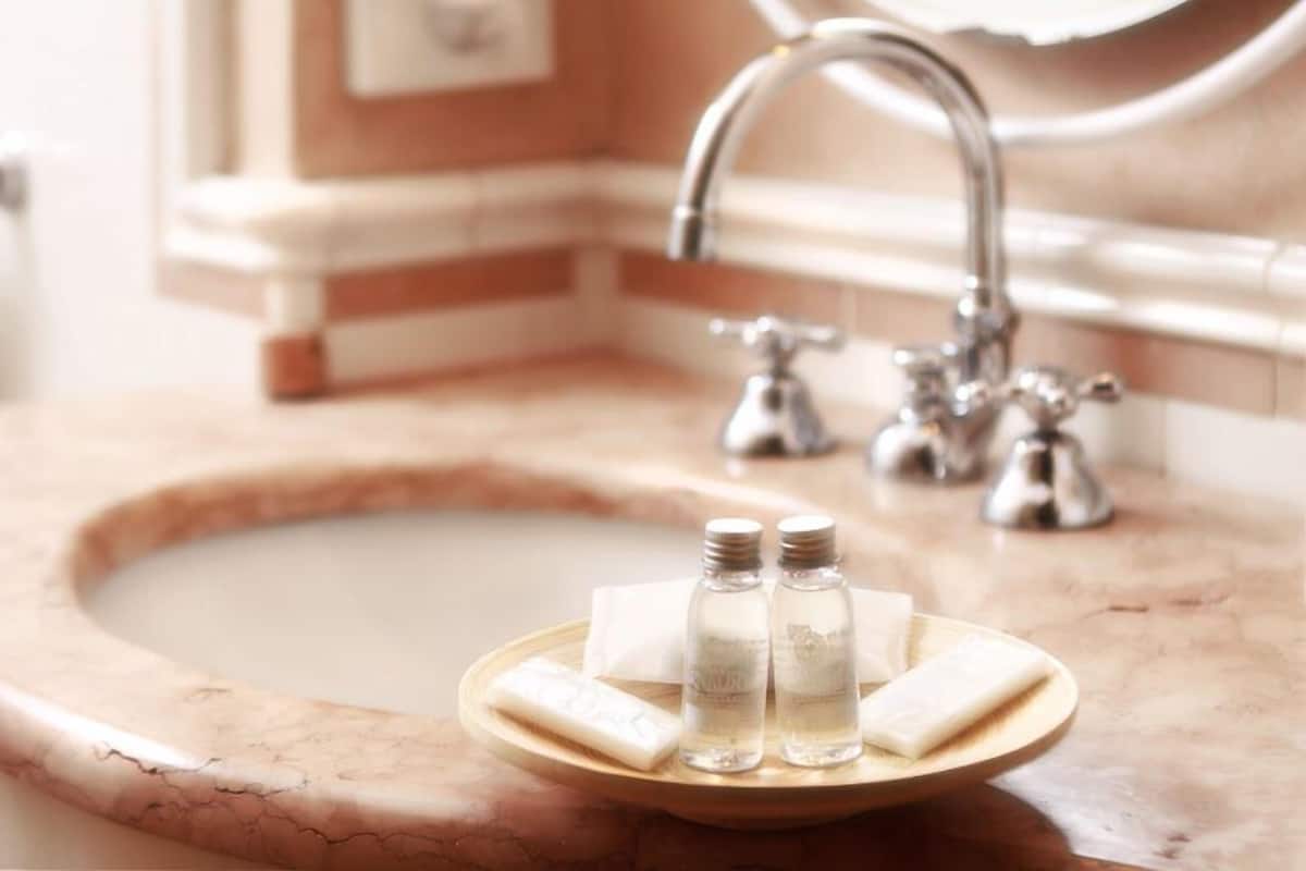 Un lavabo de salle de bain avec un receveur en marbre, deux flacons de savon liquide et un pain de savon posés sur un plateau en bois.
