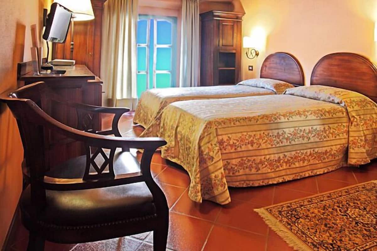Une chambre avec deux lits, un bureau, une chaise et une fenêtre avec des rideaux.