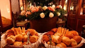 A table with baskets of bread and pastries, surrounded by chairs and a floral arrangement. - Hotel Arnaldo Aquila d'Oro (Rubiera)