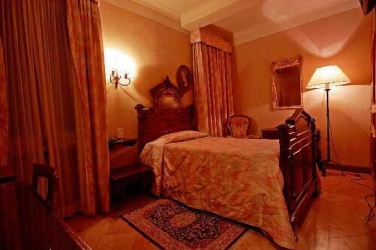 Une pièce comprenant un lit, un bureau, une chaise, une lampe et une fenêtre avec des rideaux.